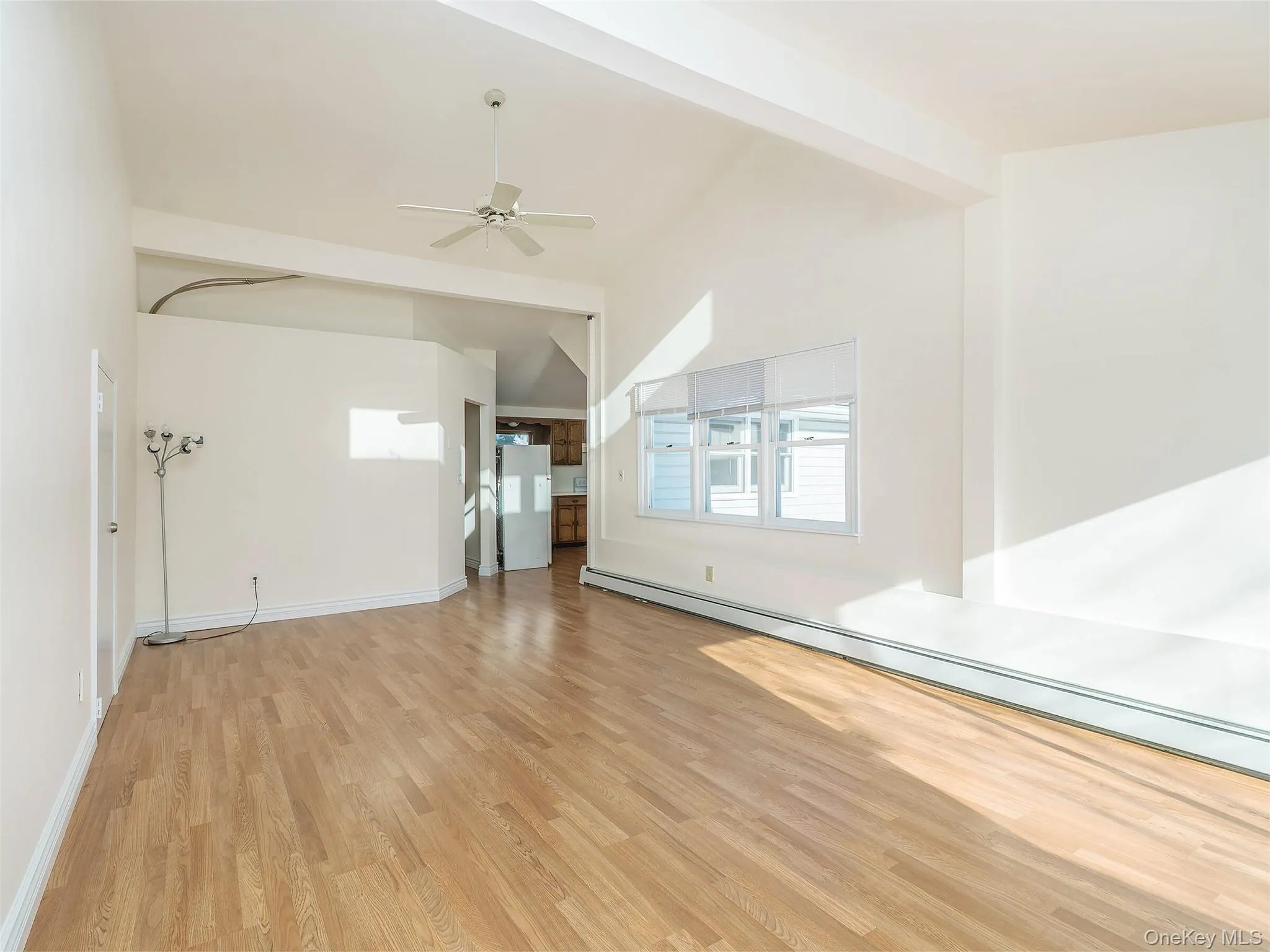 Unfurnished living room with a baseboard radiator, light wood finished floors, a ceiling fan, and lofted ceiling Unfurnished living room with a baseboard radiator, light wood finished floors, a ceiling fan, and lofted ceiling