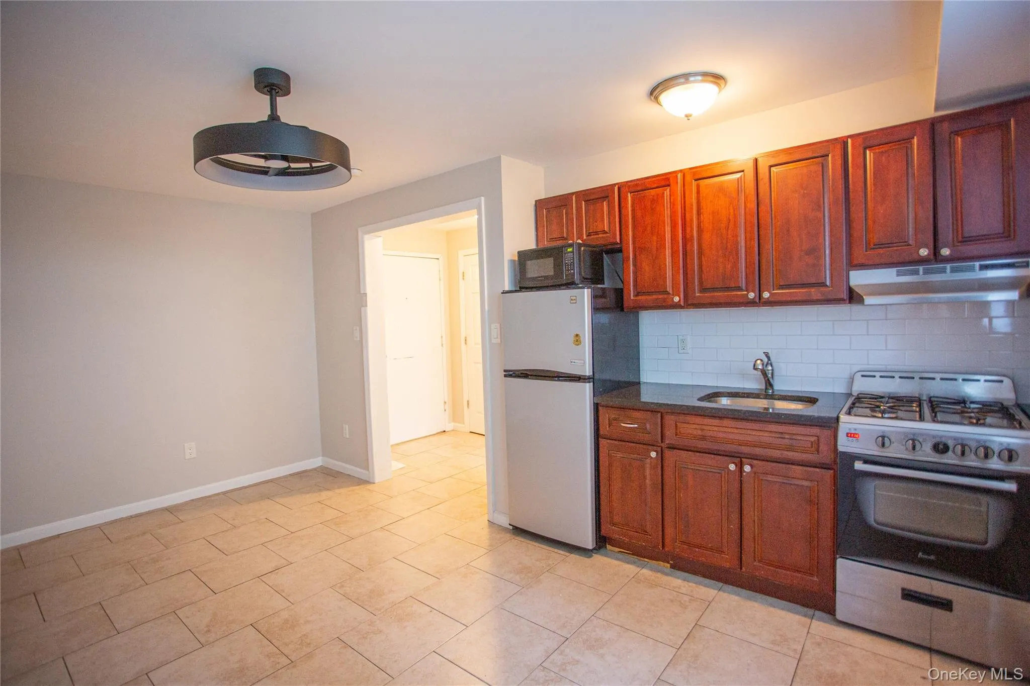 Kitchen with stainless steel appliances, dark stone countertops, under cabinet range hood, decorative backsplash, and brown cabinets Kitchen with stainless steel appliances, dark stone countertops, under cabinet range hood, decorative backsplash, and brown cabinets