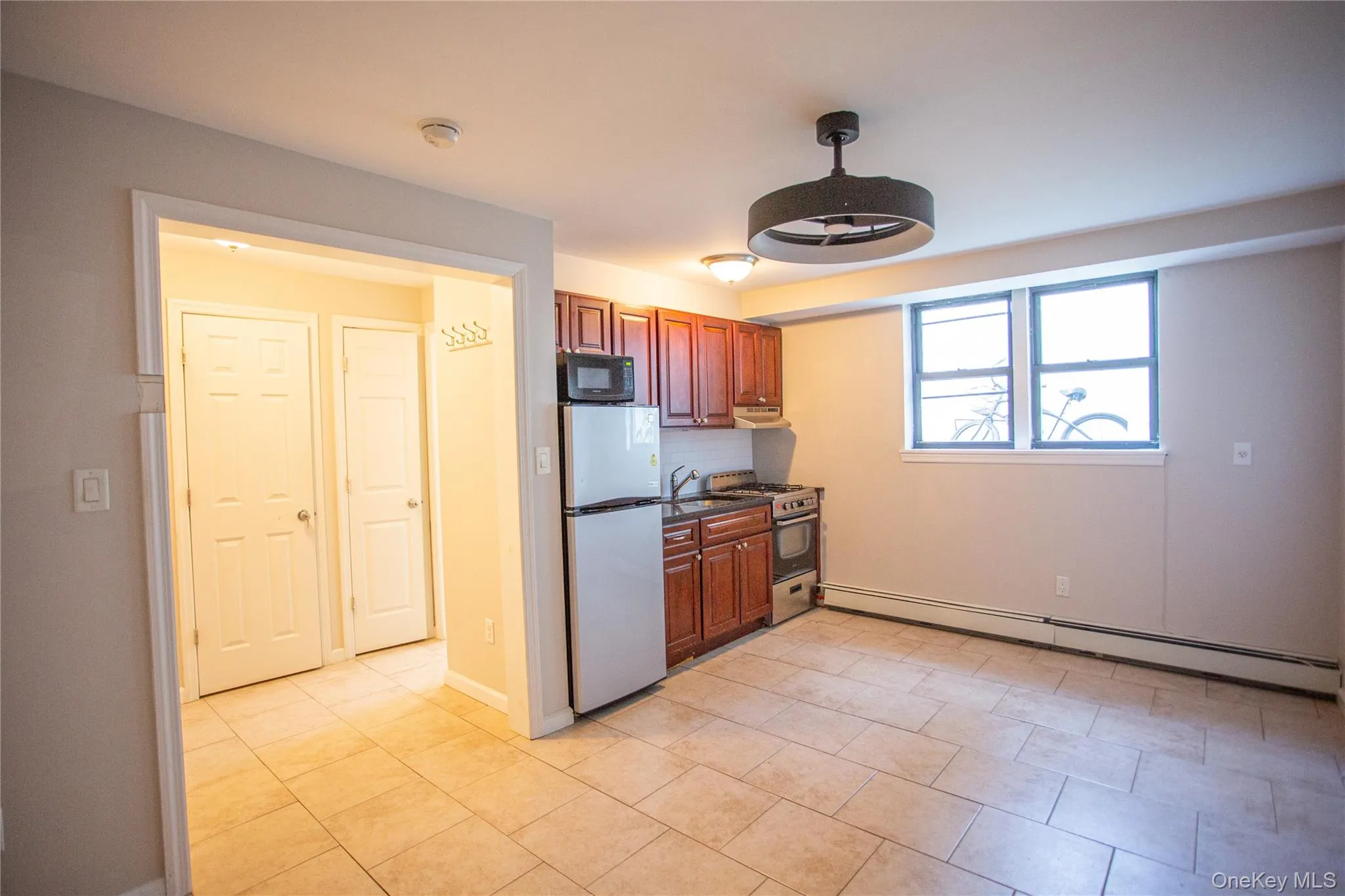 Kitchen with stainless steel appliances, a baseboard radiator, decorative backsplash, dark stone counters, and light tile patterned floors Kitchen with stainless steel appliances, a baseboard radiator, decorative backsplash, dark stone counters, and light tile patterned floors