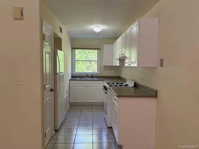Kitchen featuring white cabinetry, white appliances, dark countertops, and light tile patterned floors Kitchen featuring white cabinetry, white appliances, dark countertops, and light tile patterned floors