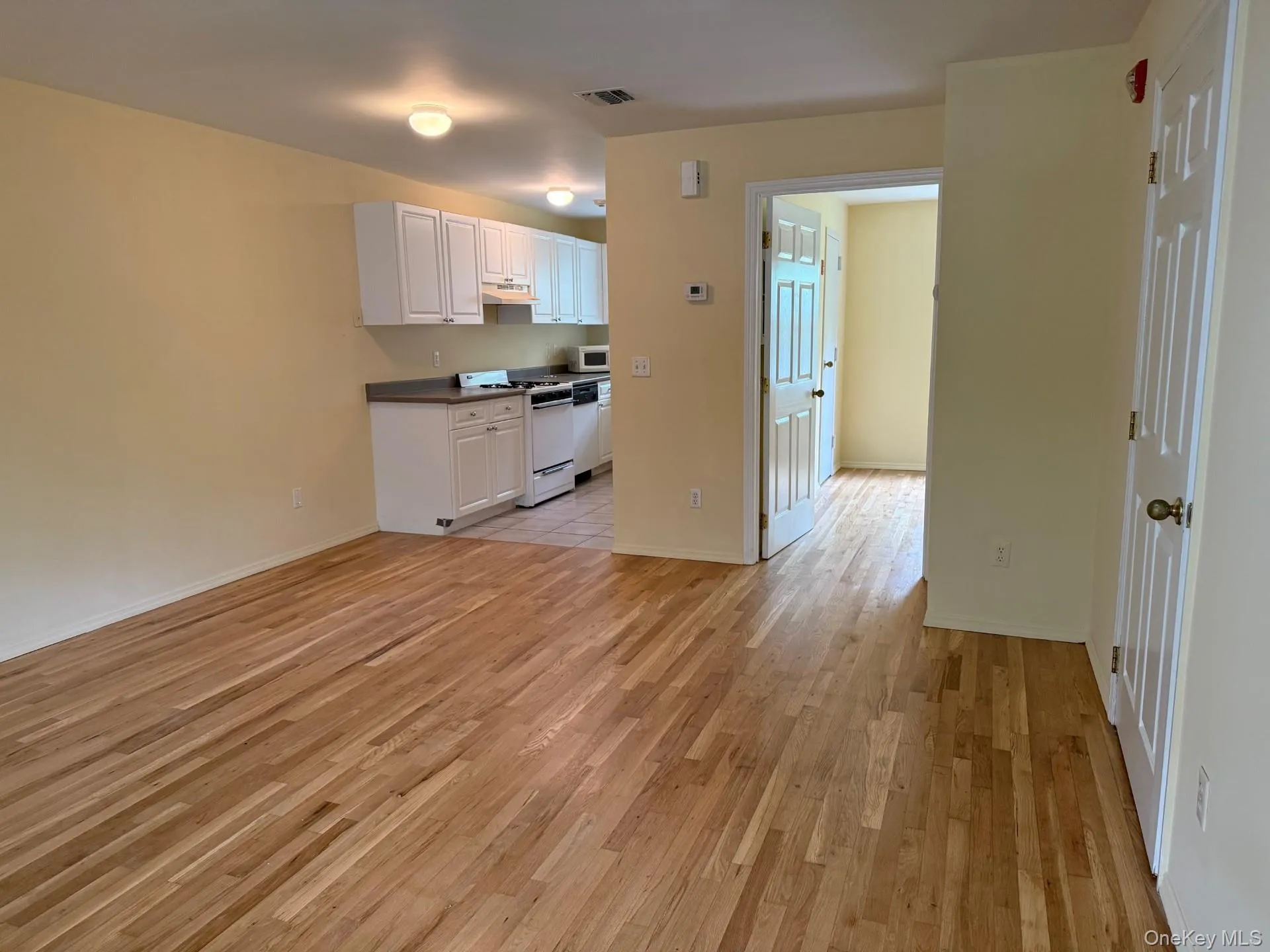 Kitchen with white cabinets, white appliances, dark countertops, light wood-type flooring, and open floor plan Kitchen with white cabinets, white appliances, dark countertops, light wood-type flooring, and open floor plan