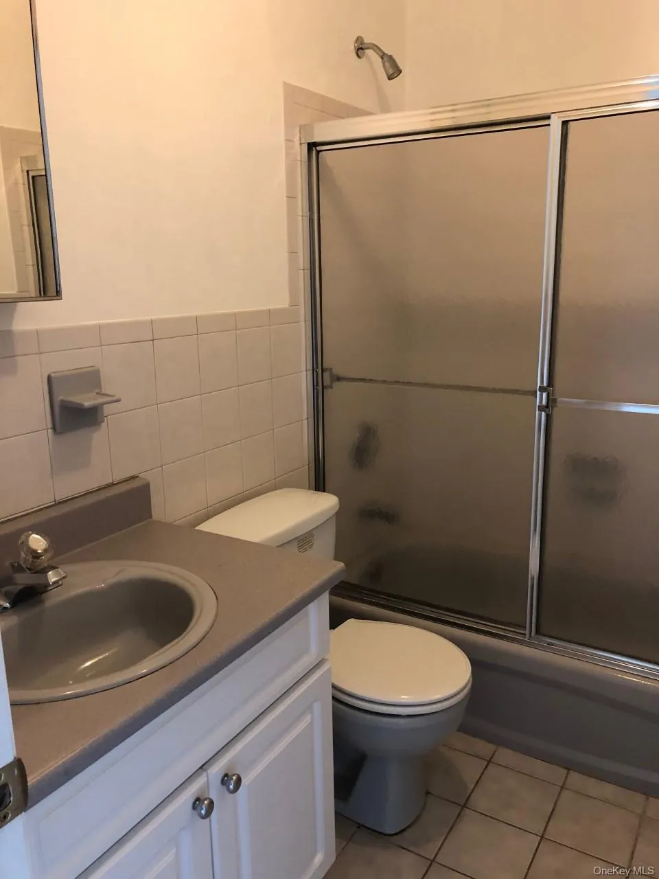 Bathroom with vanity, shower / bath combination with glass door, light tile patterned flooring, and tile walls Bathroom with vanity, shower / bath combination with glass door, light tile patterned flooring, and tile walls