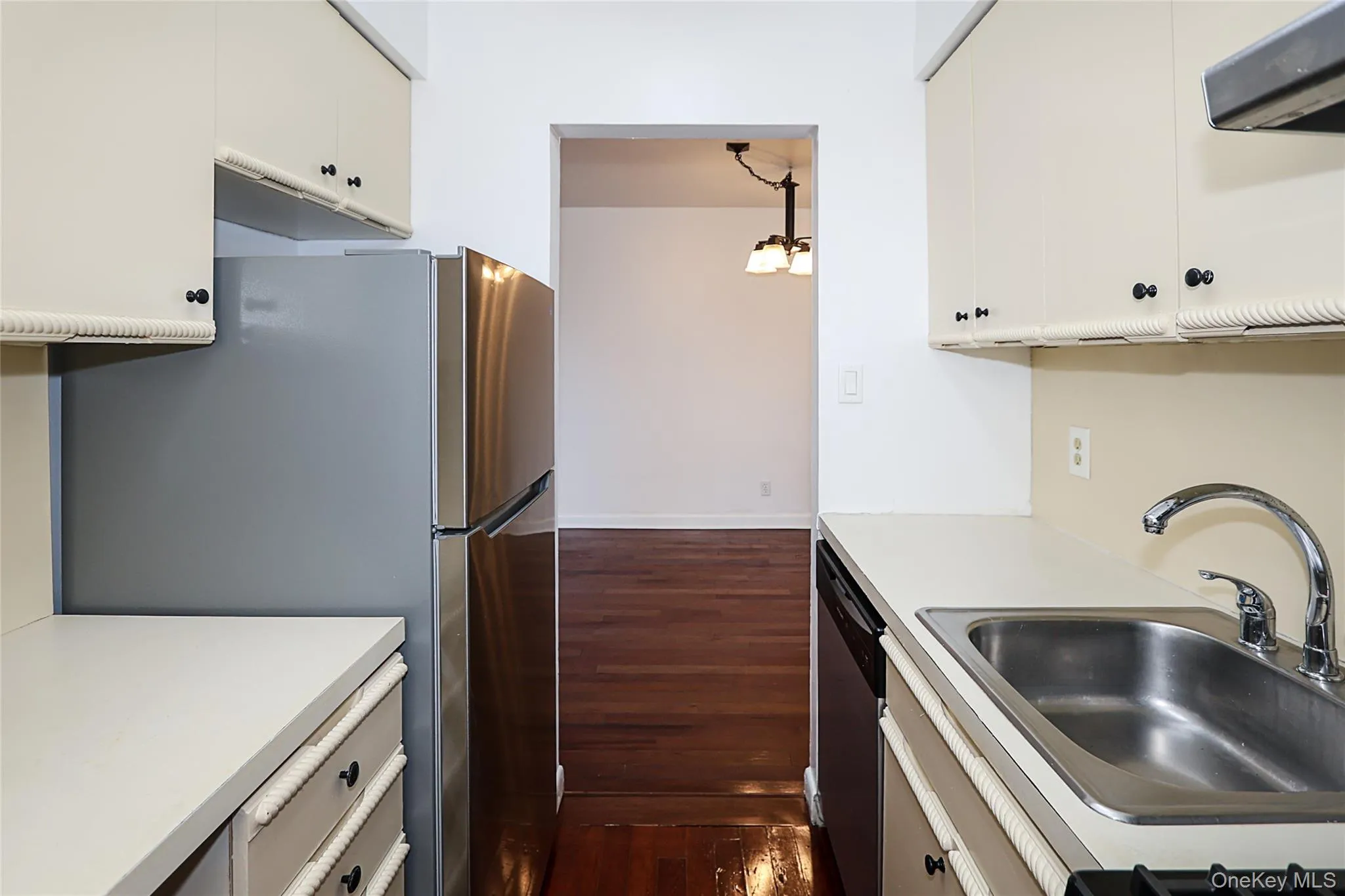 Kitchen with light countertops, exhaust hood, stainless steel appliances, dark wood-style flooring, and a chandelier Kitchen with light countertops, exhaust hood, stainless steel appliances, dark wood-style flooring, and a chandelier