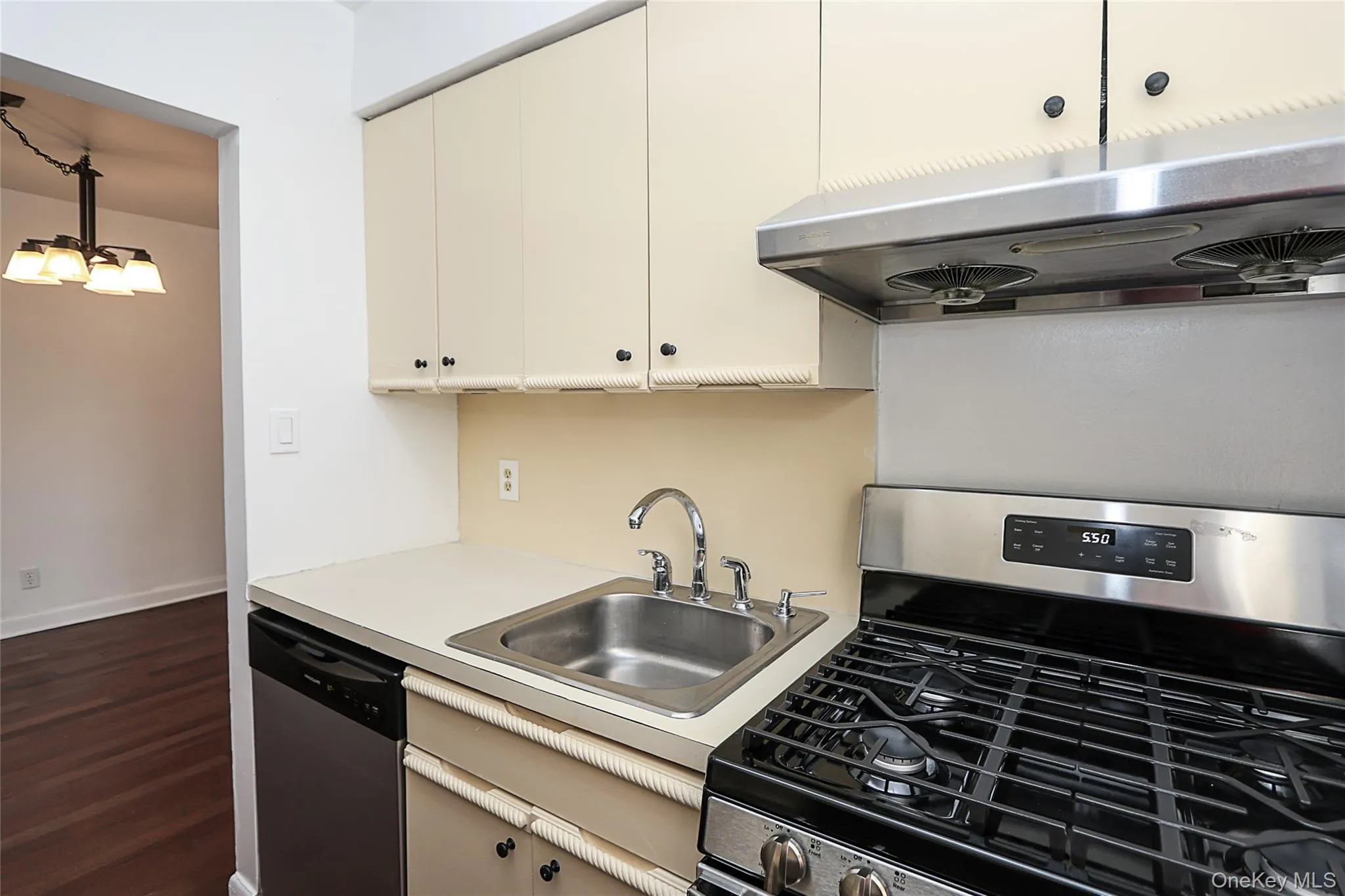 Kitchen featuring appliances with stainless steel finishes, light countertops, under cabinet range hood, decorative light fixtures, and dark wood-type flooring Kitchen featuring appliances with stainless steel finishes, light countertops, under cabinet range hood, decorative light fixtures, and dark wood-type flooring