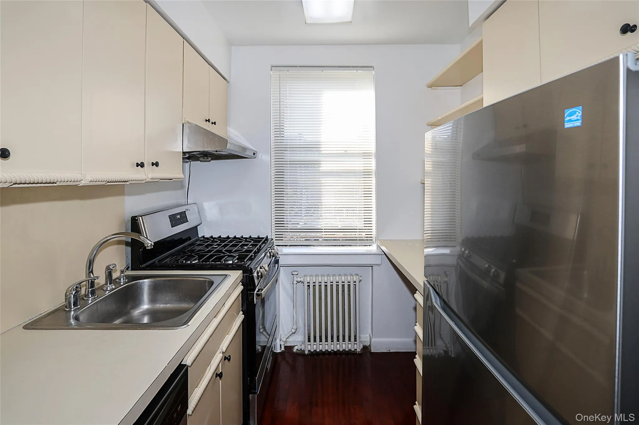 Kitchen with stainless steel appliances, radiator heating unit, light countertops, under cabinet range hood, and open shelves Kitchen with stainless steel appliances, radiator heating unit, light countertops, under cabinet range hood, and open shelves
