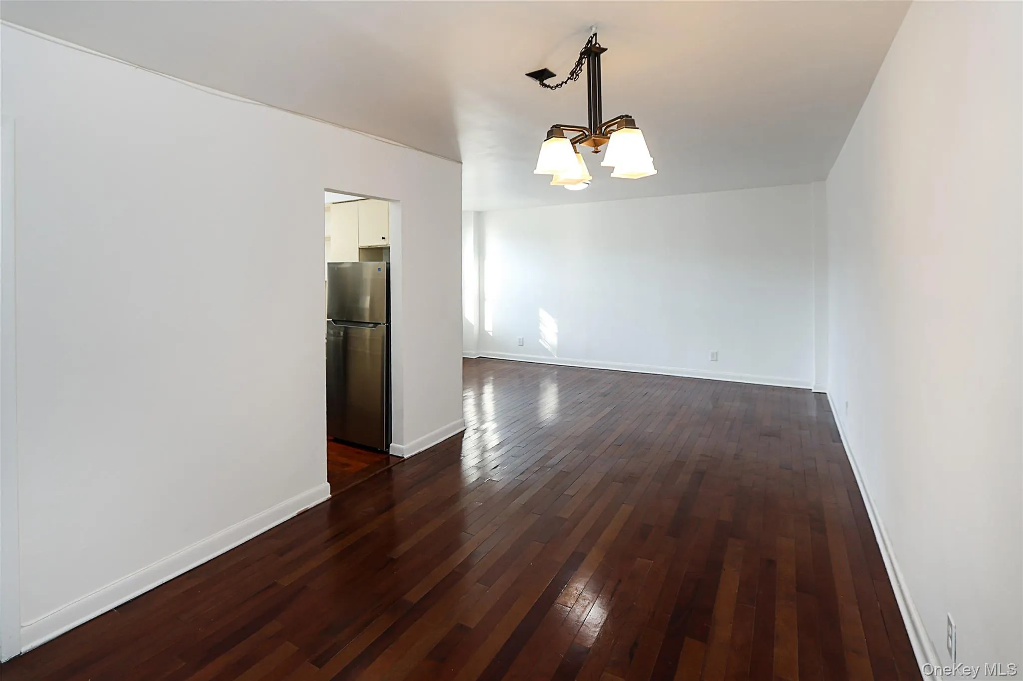 Empty room with a chandelier and dark wood-style flooring Empty room with a chandelier and dark wood-style flooring