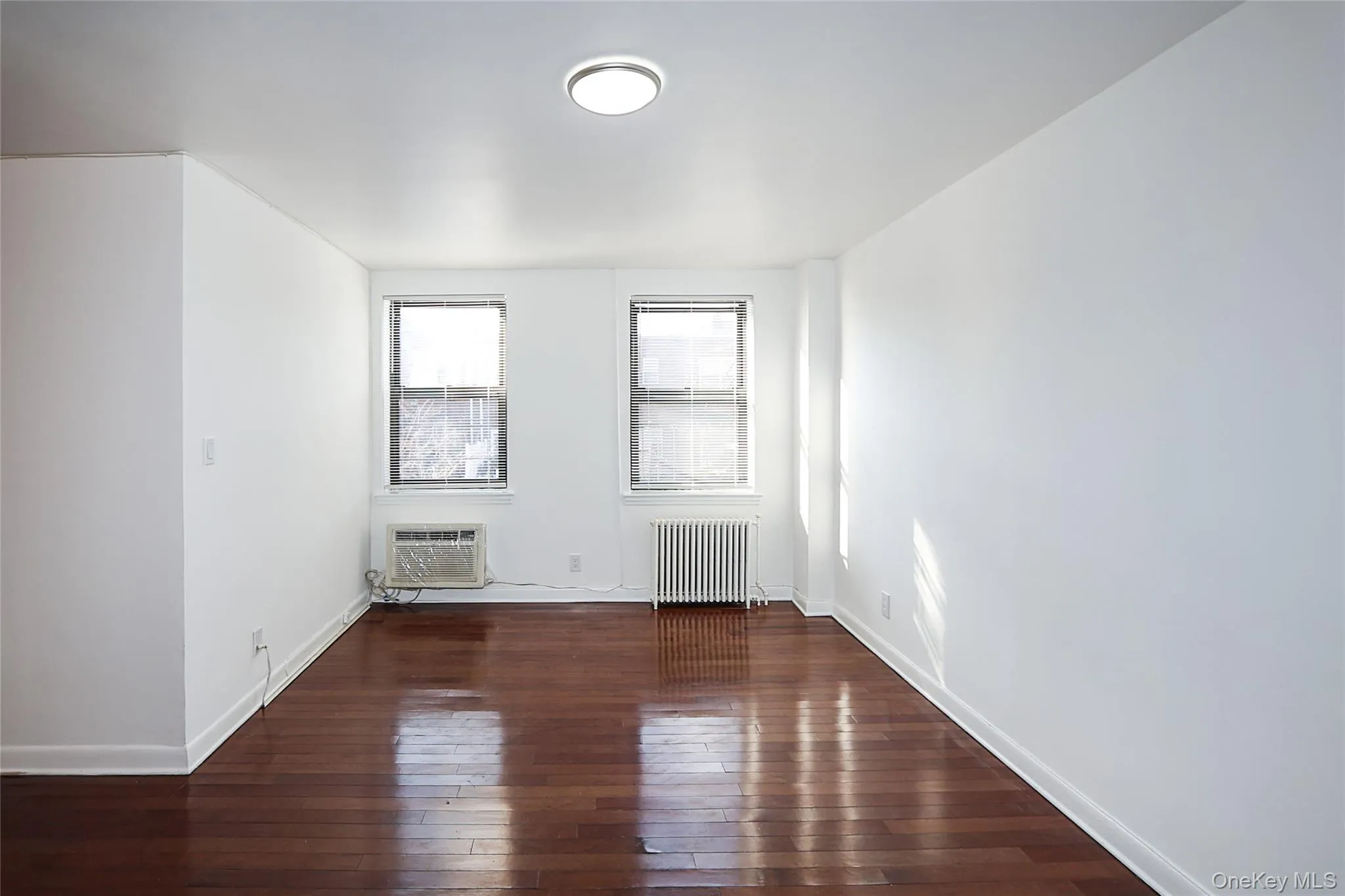 Unfurnished room with dark wood-style flooring, radiator heating unit, and a wall mounted AC Unfurnished room with dark wood-style flooring, radiator heating unit, and a wall mounted AC