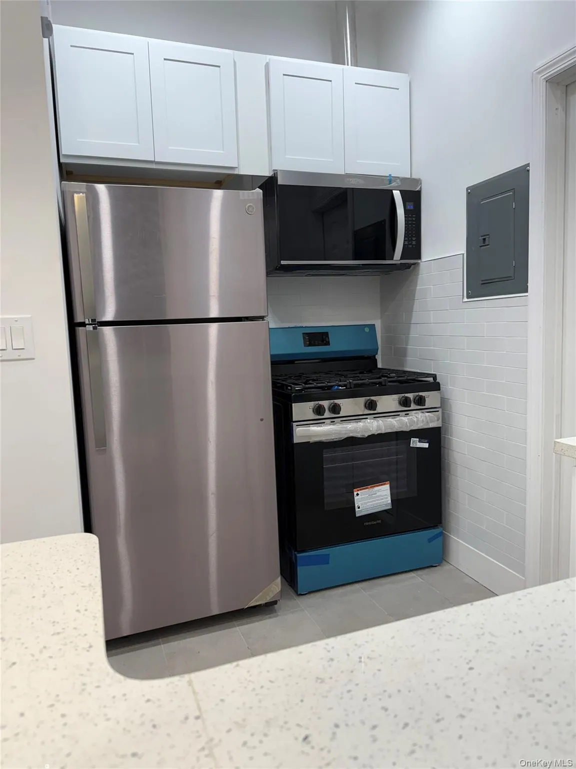 Kitchen featuring stainless steel appliances, electric panel, light tile patterned floors, white cabinetry, and tile walls Kitchen featuring stainless steel appliances, electric panel, light tile patterned floors, white cabinetry, and tile walls