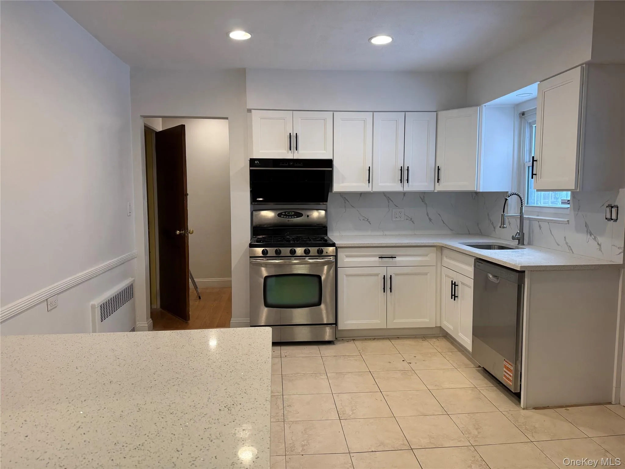 Kitchen with white cabinets, light stone countertops, stainless steel appliances, tasteful backsplash, and radiator heating unit Kitchen with white cabinets, light stone countertops, stainless steel appliances, tasteful backsplash, and radiator heating unit