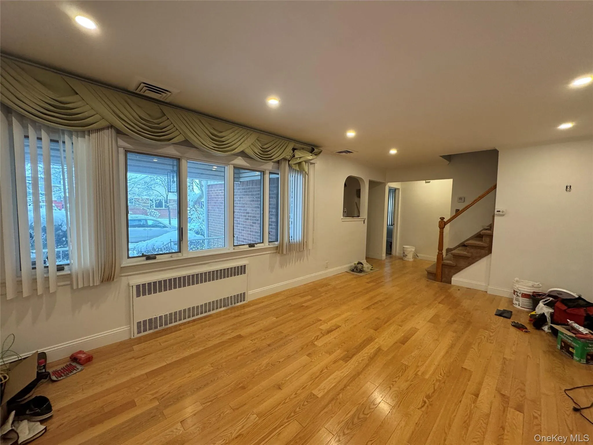 Unfurnished living room with radiator, light wood-style floors, recessed lighting, stairs, and arched walkways Unfurnished living room with radiator, light wood-style floors, recessed lighting, stairs, and arched walkways