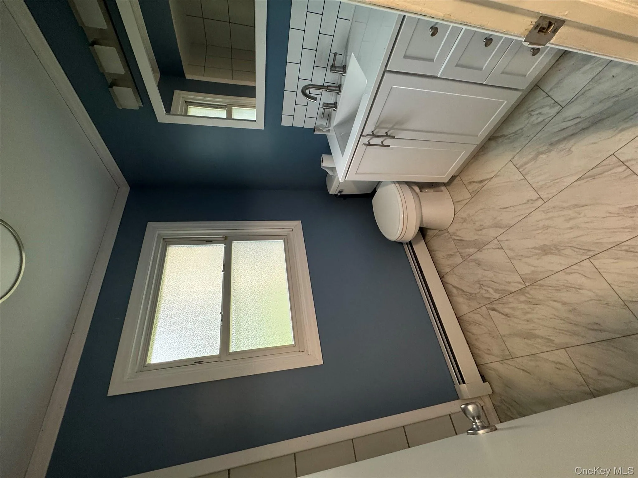 Half bath with vanity, a baseboard radiator, decorative backsplash, crown molding, and light marble finish flooring Half bath with vanity, a baseboard radiator, decorative backsplash, crown molding, and light marble finish flooring