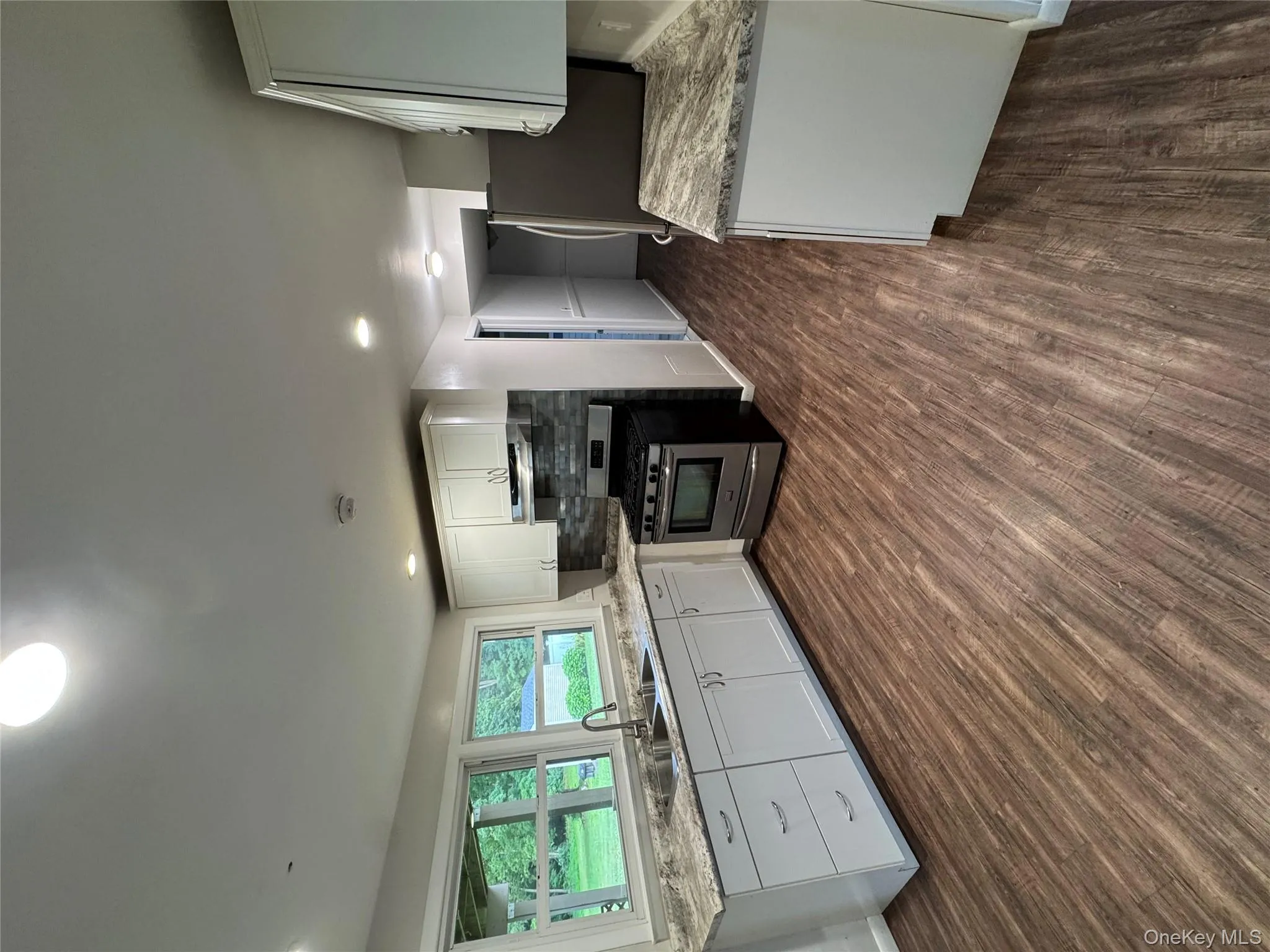 Kitchen with white cabinetry, stainless steel range with gas cooktop, light stone counters, backsplash, and dark wood-style flooring Kitchen with white cabinetry, stainless steel range with gas cooktop, light stone counters, backsplash, and dark wood-style flooring