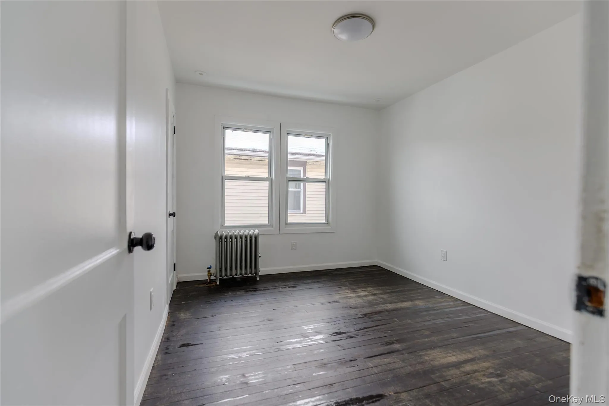 Unfurnished room featuring radiator and dark wood-style flooring Unfurnished room featuring radiator and dark wood-style flooring