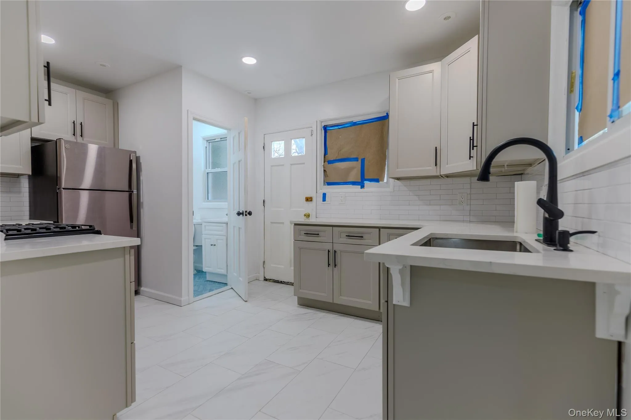 Kitchen featuring backsplash, light stone countertops, recessed lighting, light marble finish floors, and freestanding refrigerator Kitchen featuring backsplash, light stone countertops, recessed lighting, light marble finish floors, and freestanding refrigerator