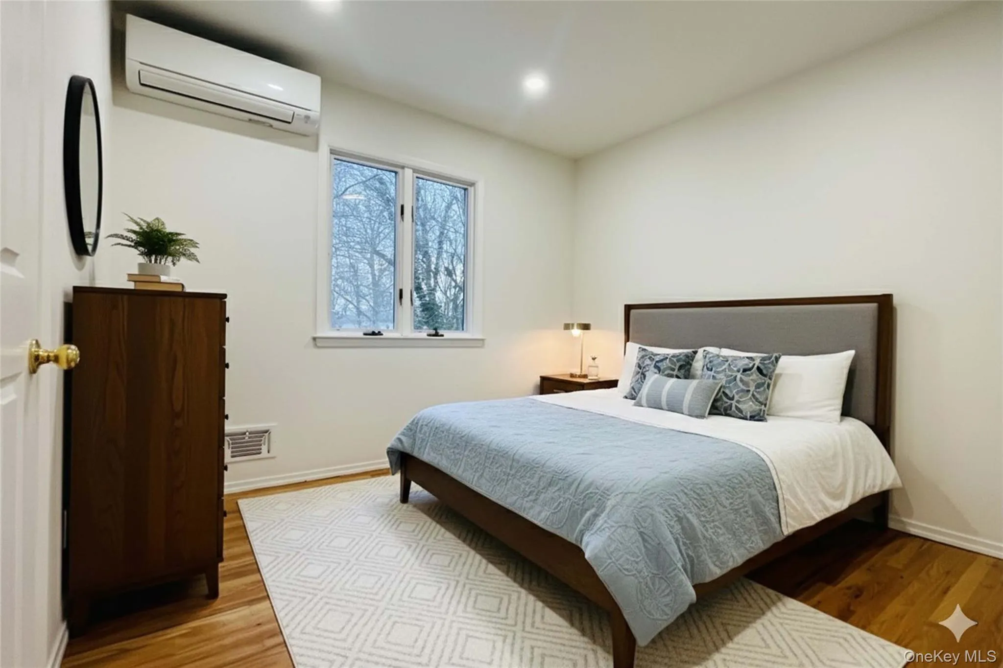 Bedroom with en-suite bath virtually staged with a wall mounted AC and light wood-style flooring Bedroom with en-suite bath virtually staged with a wall mounted AC and light wood-style flooring