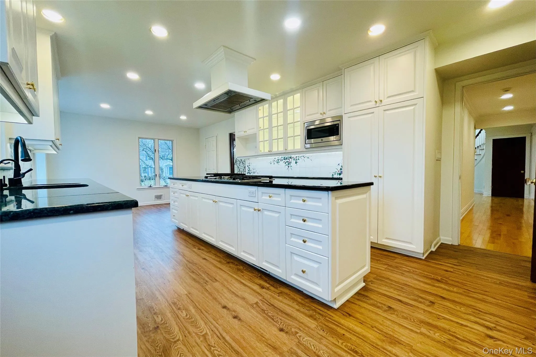 Kitchen with light wood finished floors, white cabinets, island exhaust hood, and recessed lighting Kitchen with light wood finished floors, white cabinets, island exhaust hood, and recessed lighting