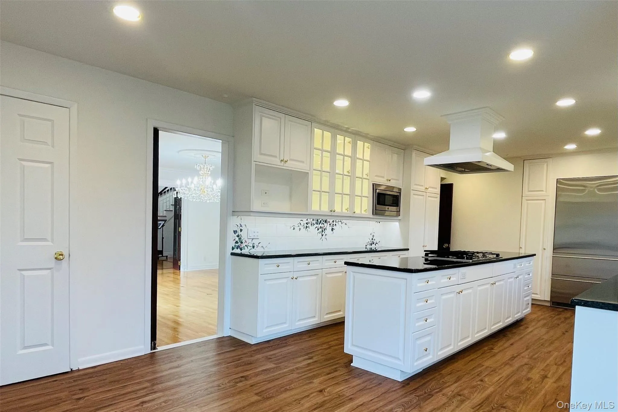 Kitchen with white cabinetry, appliances with stainless steel finishes, extractor fan, glass insert cabinets, and dark wood-type flooring Kitchen with white cabinetry, appliances with stainless steel finishes, extractor fan, glass insert cabinets, and dark wood-type flooring