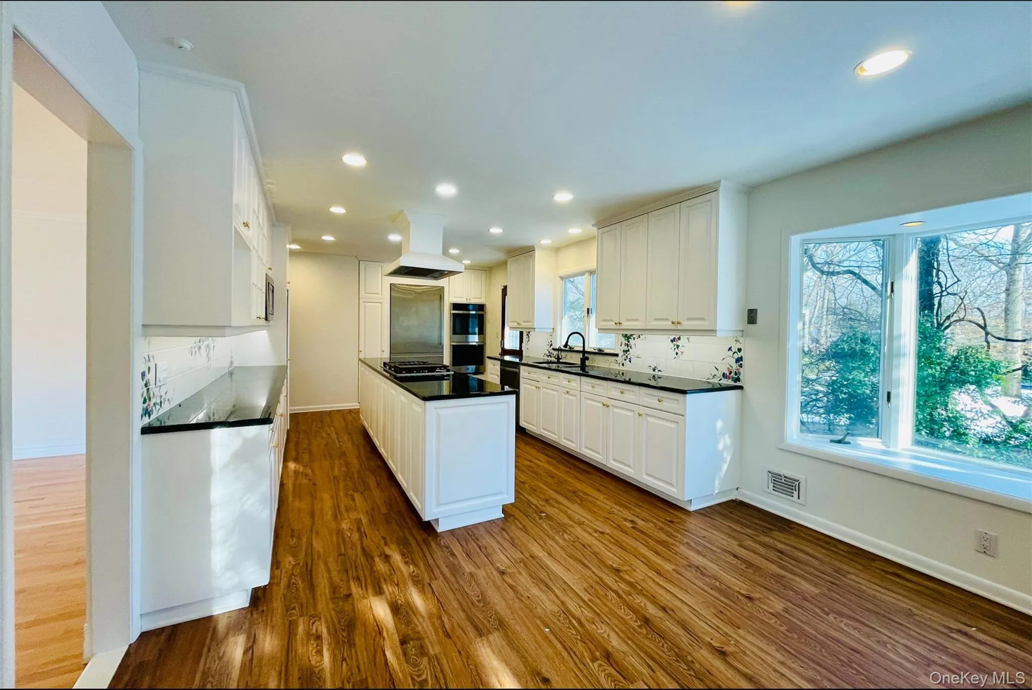 Kitchen with tasteful backsplash, a center island, white cabinetry, dark wood finished floors, and premium range hood Kitchen with tasteful backsplash, a center island, white cabinetry, dark wood finished floors, and premium range hood