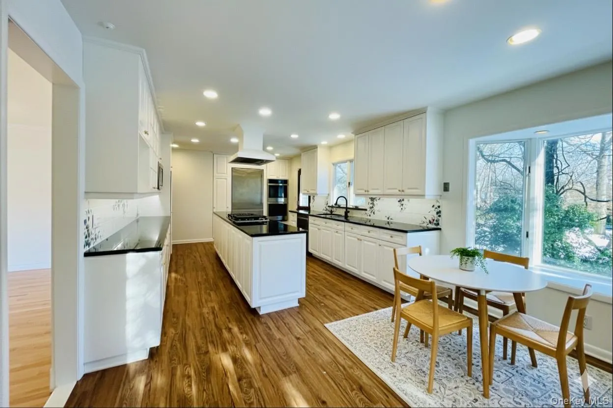 Virtually staged Kitchen featuring decorative backsplash, a kitchen island, white cabinets, custom range hood, and dark wood-style floors Virtually staged Kitchen featuring decorative backsplash, a kitchen island, white cabinets, custom range hood, and dark wood-style floors