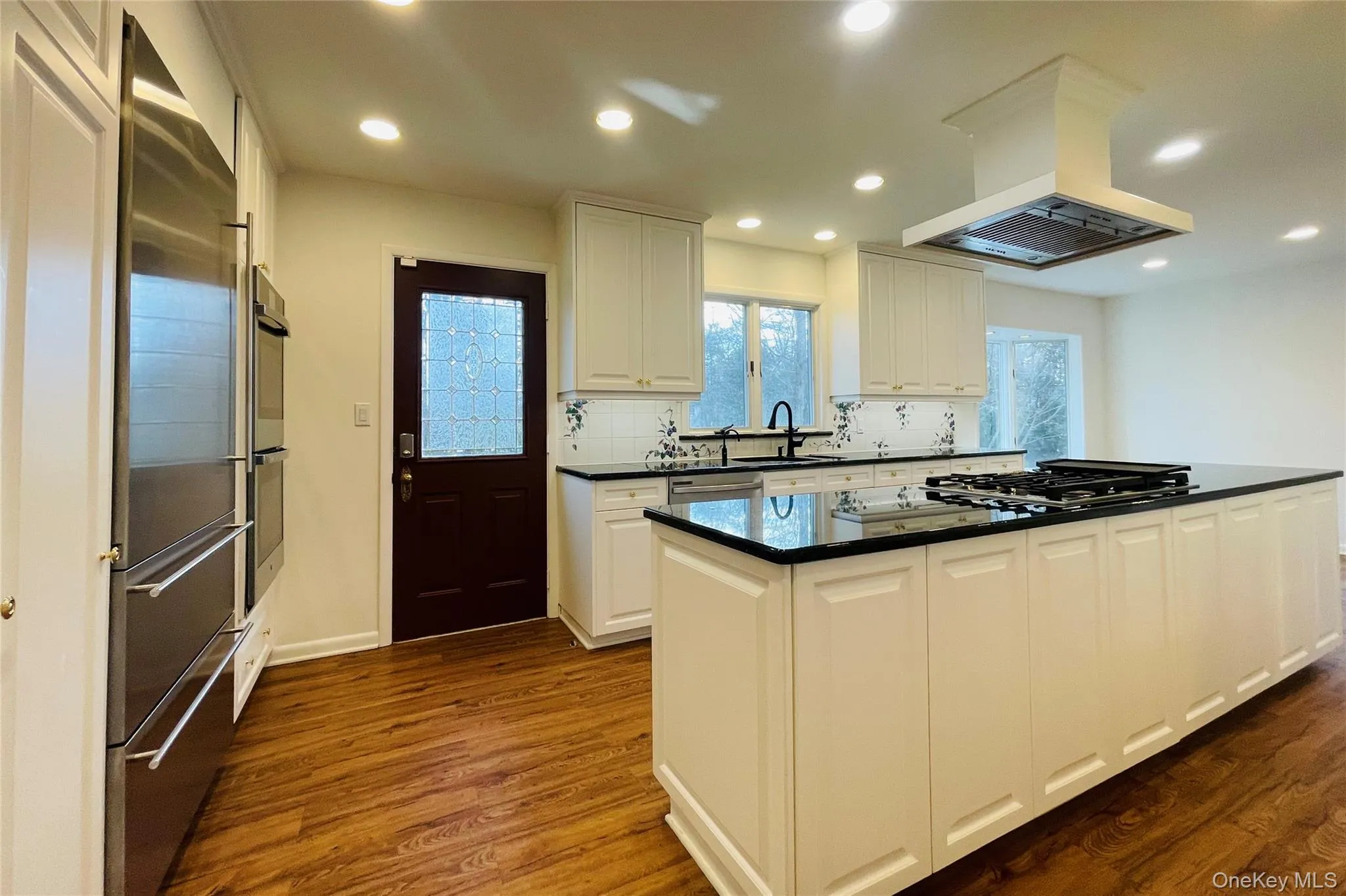 Kitchen featuring white cabinets, stainless steel appliances, island range hood, a kitchen island, and dark wood-type flooring Kitchen featuring white cabinets, stainless steel appliances, island range hood, a kitchen island, and dark wood-type flooring