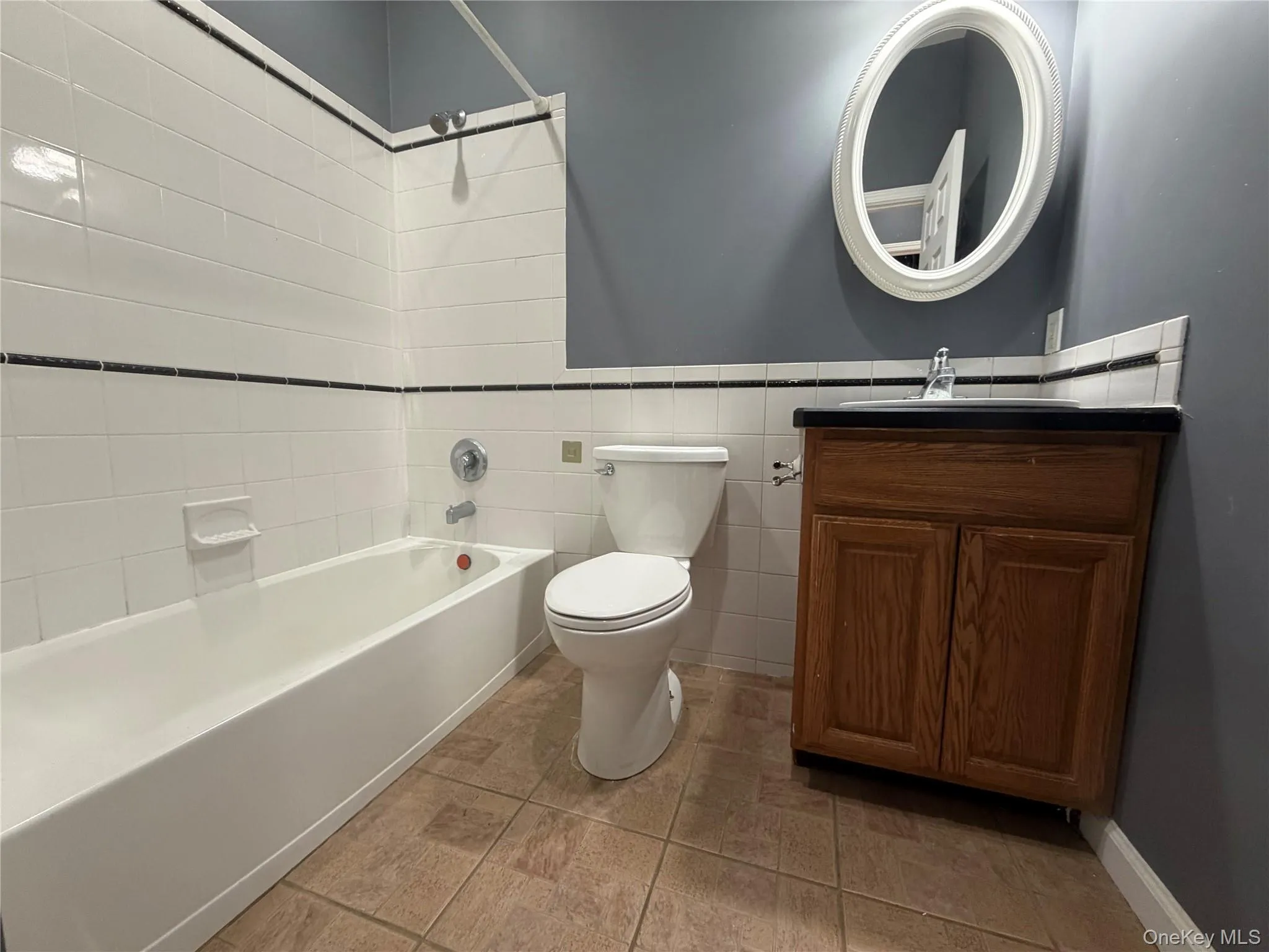 Bathroom with vanity, shower / tub combination, tile walls, wainscoting, and light tile patterned floors Bathroom with vanity, shower / tub combination, tile walls, wainscoting, and light tile patterned floors