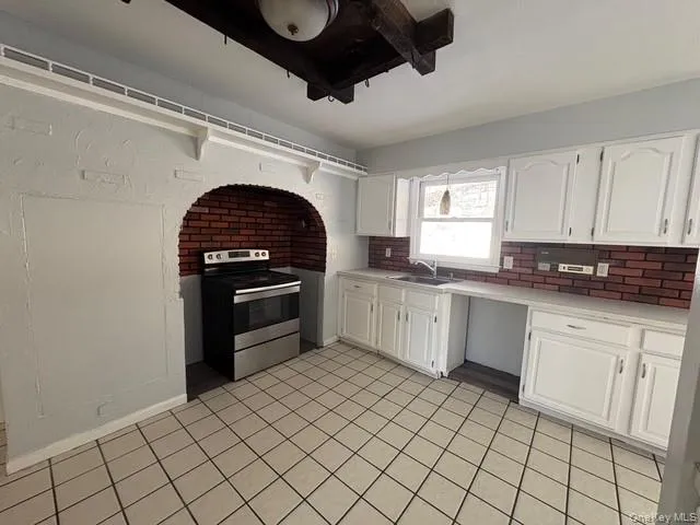 Kitchen featuring stainless steel range with electric cooktop, white cabinets, light countertops, light tile patterned floors, and tasteful backsplash Kitchen featuring stainless steel range with electric cooktop, white cabinets, light countertops, light tile patterned floors, and tasteful backsplash