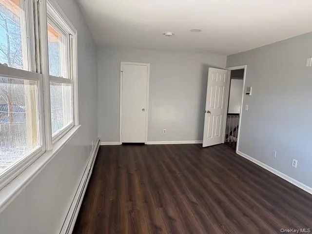 Unfurnished bedroom with a baseboard radiator and dark wood-style flooring Unfurnished bedroom with a baseboard radiator and dark wood-style flooring