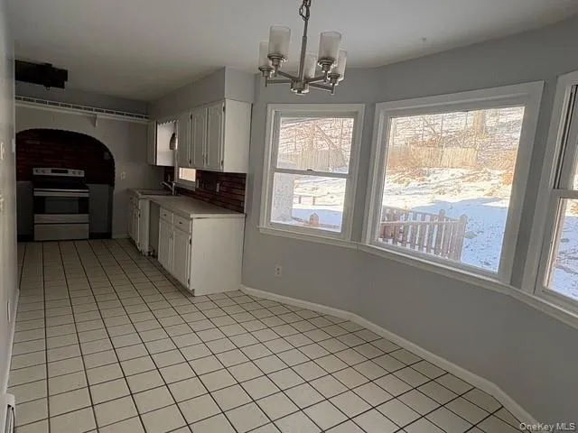Kitchen featuring white cabinetry, electric range, decorative light fixtures, a chandelier, and light countertops Kitchen featuring white cabinetry, electric range, decorative light fixtures, a chandelier, and light countertops