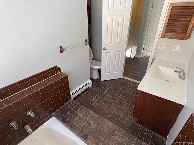 Full bathroom with double vanity, a bath, brick patterned flooring, and a baseboard radiator Full bathroom with double vanity, a bath, brick patterned flooring, and a baseboard radiator