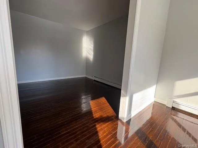 Unfurnished room with dark wood-style flooring and a baseboard heating unit Unfurnished room with dark wood-style flooring and a baseboard heating unit