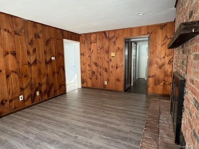 Spare room with wood walls, a brick fireplace, and dark wood-type flooring Spare room with wood walls, a brick fireplace, and dark wood-type flooring