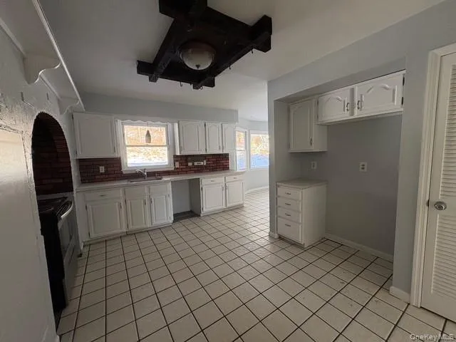 Kitchen featuring white cabinetry, light countertops, black range with electric cooktop, and light tile patterned flooring Kitchen featuring white cabinetry, light countertops, black range with electric cooktop, and light tile patterned flooring