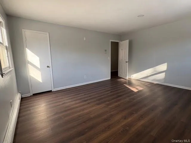 Unfurnished room with baseboard heating and dark wood finished floors Unfurnished room with baseboard heating and dark wood finished floors