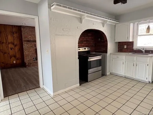 Kitchen with stainless steel electric range oven, light countertops, white cabinetry, light tile patterned floors, and brick wall Kitchen with stainless steel electric range oven, light countertops, white cabinetry, light tile patterned floors, and brick wall