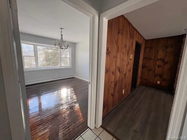 Hallway with wood walls, wood finished floors, a baseboard radiator, and a chandelier Hallway with wood walls, wood finished floors, a baseboard radiator, and a chandelier