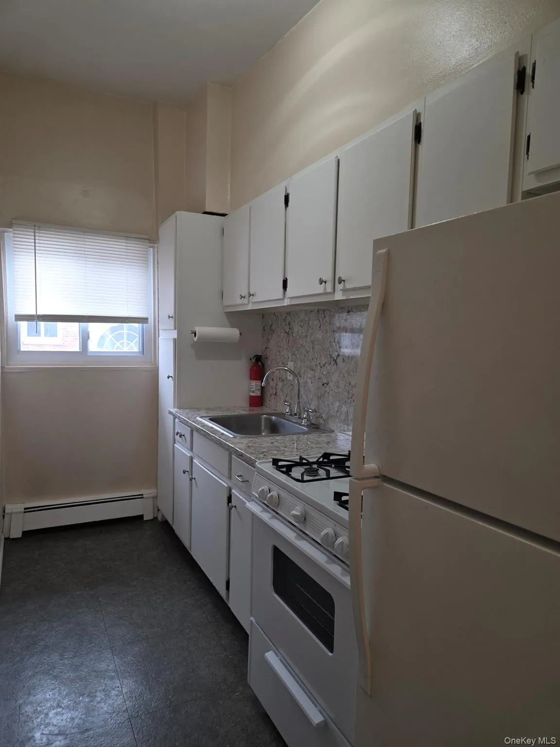 Kitchen featuring white appliances, white cabinets, light countertops, a baseboard heating unit, and tasteful backsplash Kitchen featuring white appliances, white cabinets, light countertops, a baseboard heating unit, and tasteful backsplash