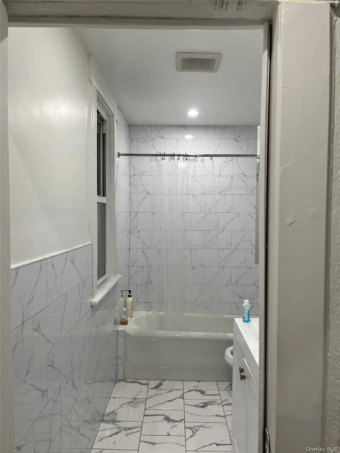 Bathroom featuring shower / bathtub combination with curtain, light marble finish floors, vanity, and tile walls Bathroom featuring shower / bathtub combination with curtain, light marble finish floors, vanity, and tile walls