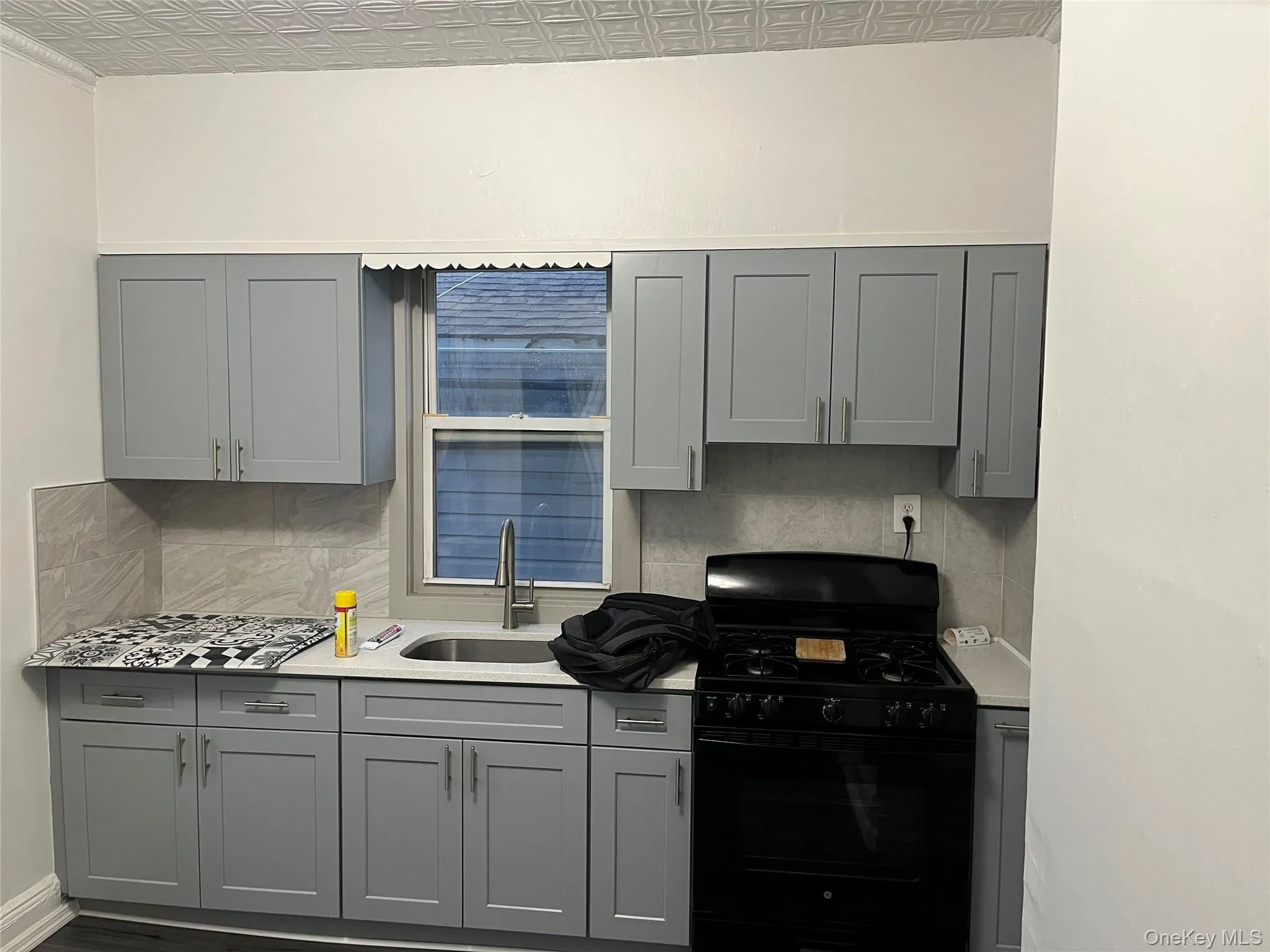 Kitchen featuring gray cabinetry, black range with gas stovetop, tasteful backsplash, an ornate ceiling, and light stone counters Kitchen featuring gray cabinetry, black range with gas stovetop, tasteful backsplash, an ornate ceiling, and light stone counters