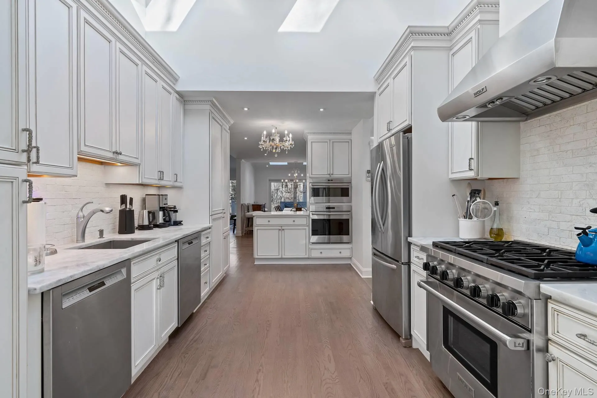 Kitchen with decorative backsplash, appliances with stainless steel finishes, exhaust hood, and a chandelier