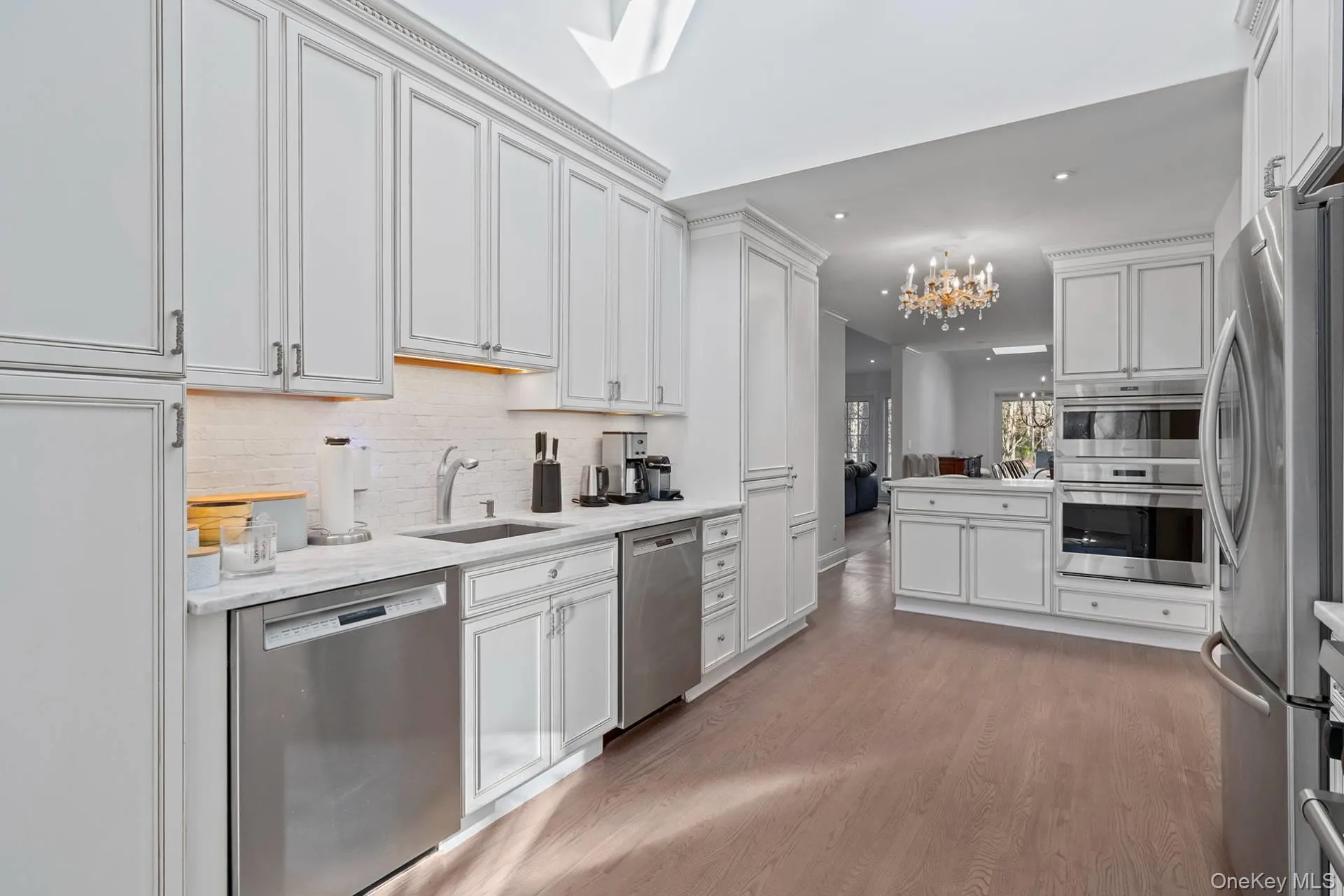 Kitchen featuring stainless steel appliances, white cabinets, a chandelier, light wood-style flooring, and tasteful backsplash