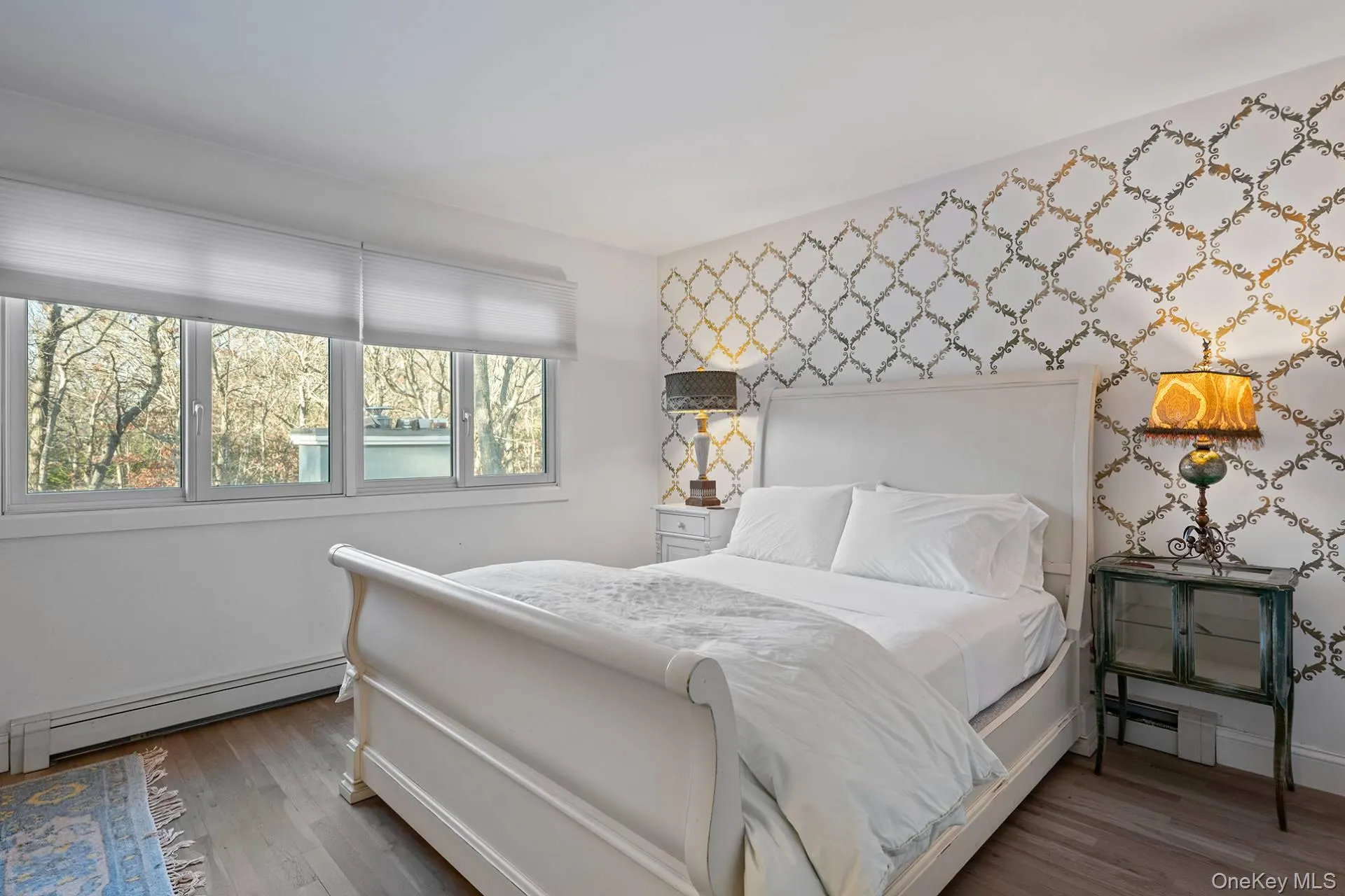 Bedroom with baseboard heating, wood finished floors, wallpapered walls, and an accent wall