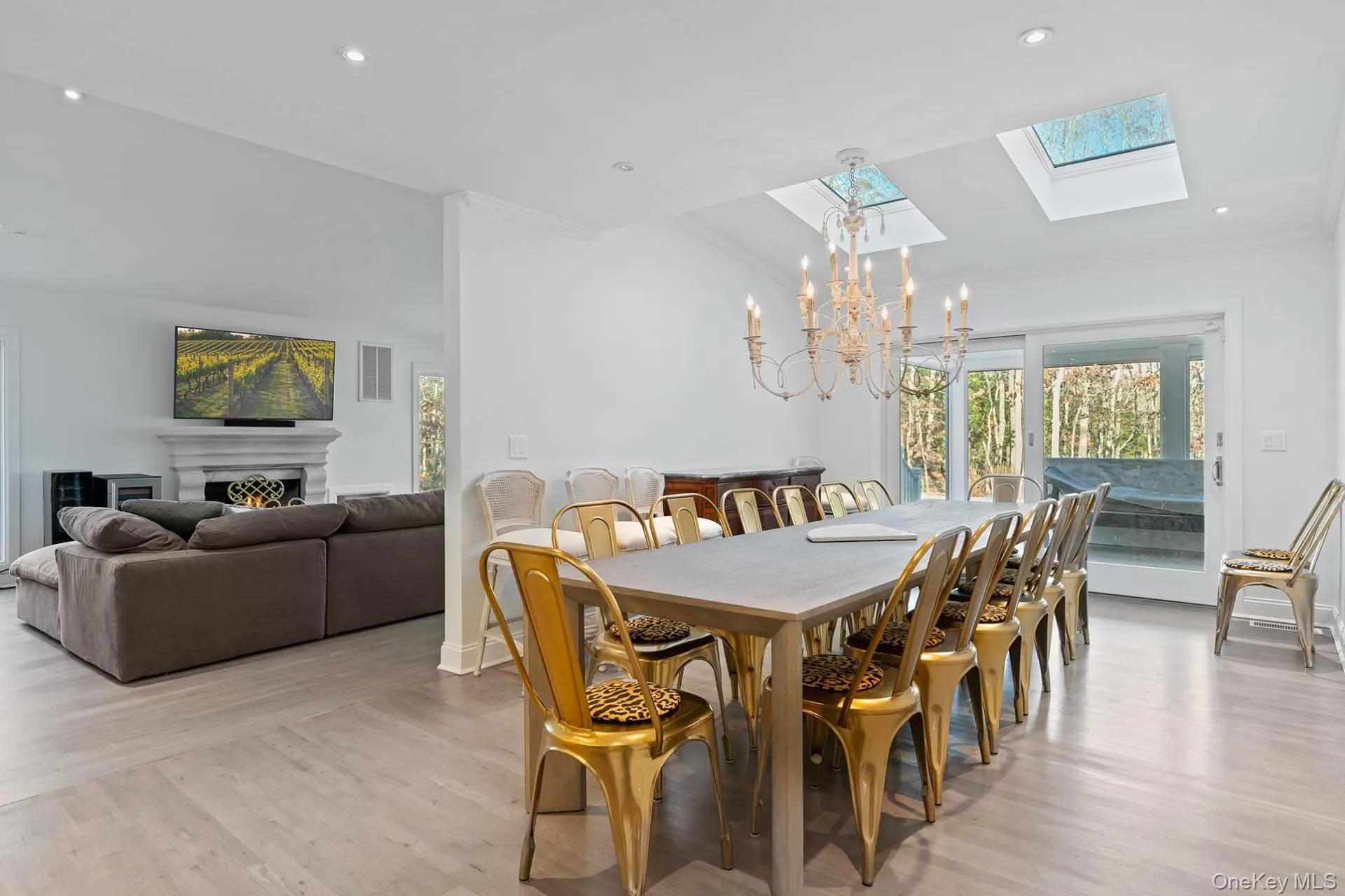 Dining area with a skylight, vaulted ceiling, light wood-type flooring, a chandelier, and a warm lit fireplace