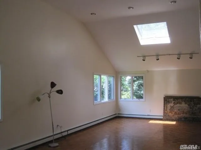 Unfurnished living room featuring healthy amount of natural light, vaulted ceiling, a skylight, a baseboard radiator, and rail lighting Unfurnished living room featuring healthy amount of natural light, vaulted ceiling, a skylight, a baseboard radiator, and rail lighting