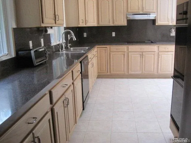 Kitchen featuring light brown cabinets, tasteful backsplash, under cabinet range hood, and light tile patterned floors Kitchen featuring light brown cabinets, tasteful backsplash, under cabinet range hood, and light tile patterned floors