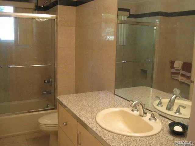 Full bathroom with shower / bath combination with glass door, vanity, and light tile patterned floors Full bathroom with shower / bath combination with glass door, vanity, and light tile patterned floors