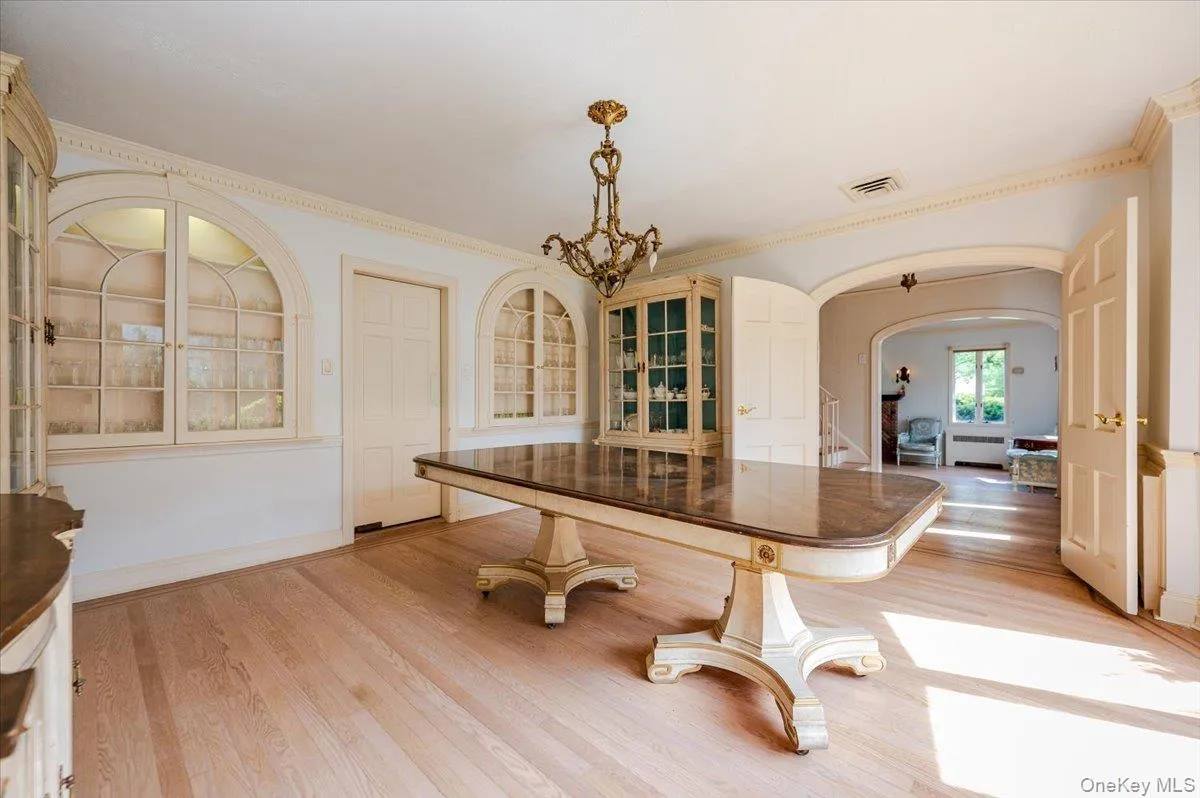 Dining room with arched walkways, light wood finished floors, a chandelier, and crown molding Dining room with arched walkways, light wood finished floors, a chandelier, and crown molding