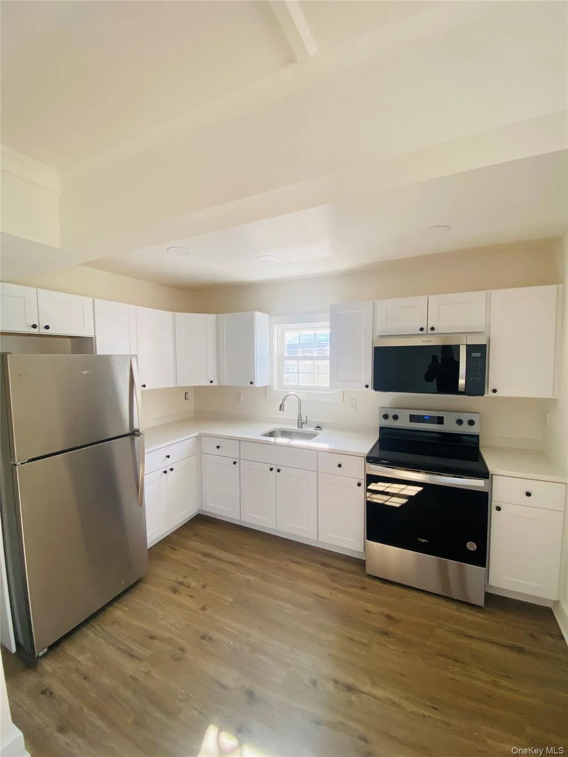 Kitchen with stainless steel appliances, white cabinets, dark wood-style flooring, and light countertops Kitchen with stainless steel appliances, white cabinets, dark wood-style flooring, and light countertops