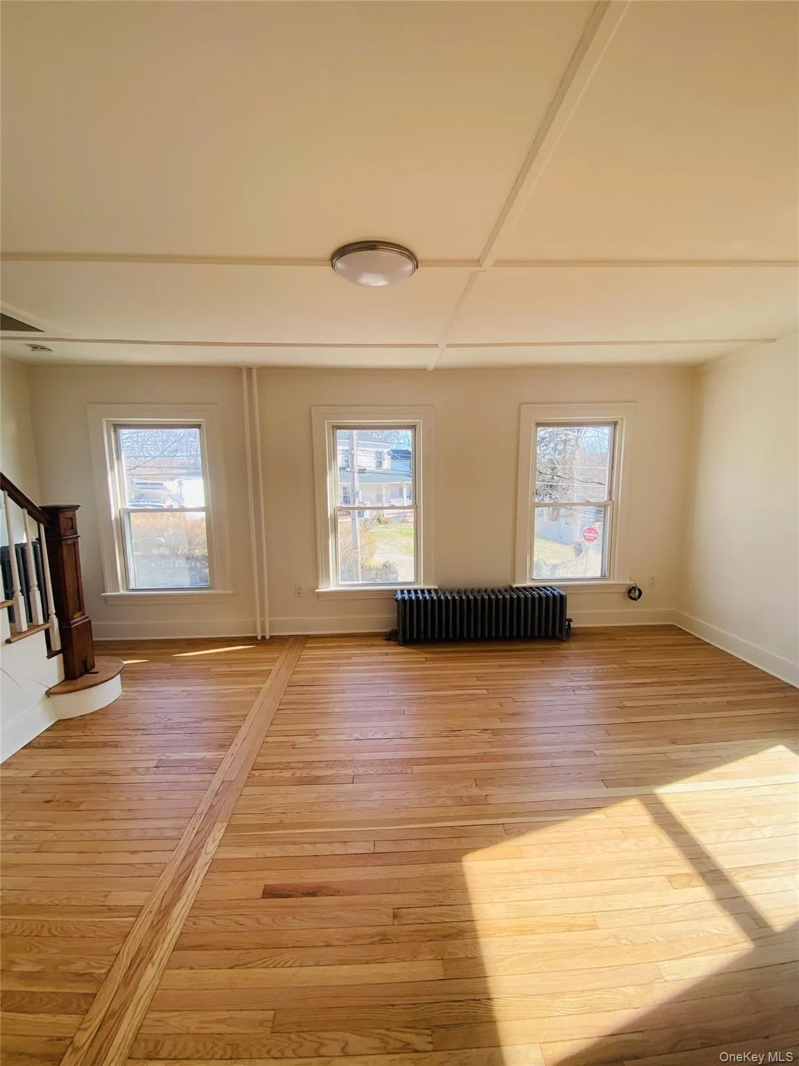 Unfurnished living room featuring stairway, radiator heating unit, plenty of natural light, and light wood finished floors Unfurnished living room featuring stairway, radiator heating unit, plenty of natural light, and light wood finished floors