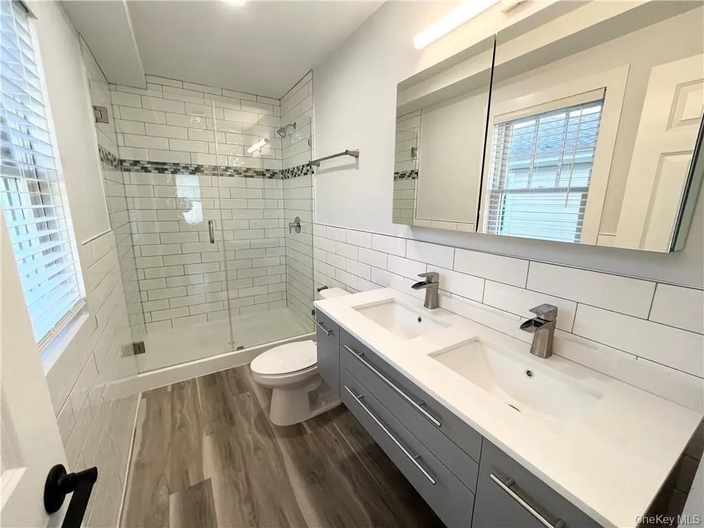 Full bath featuring double vanity, tile walls, dark wood-style floors, a stall shower, and plenty of natural light Full bath featuring double vanity, tile walls, dark wood-style floors, a stall shower, and plenty of natural light