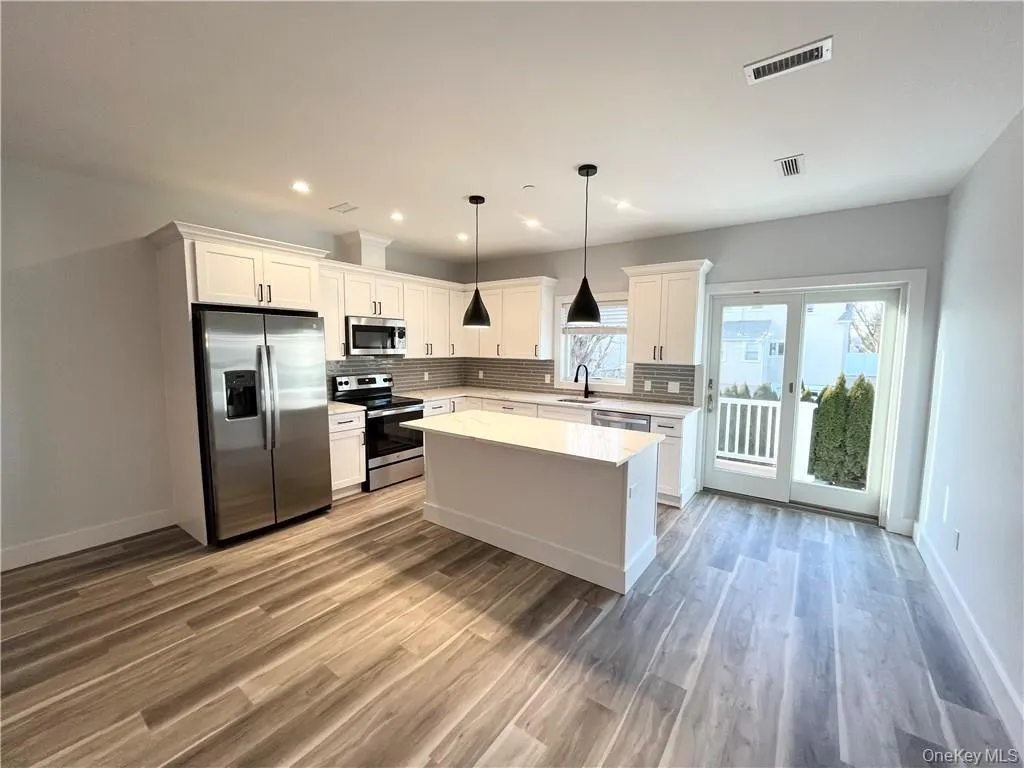 Kitchen featuring stainless steel appliances, white cabinetry, hanging light fixtures, a center island, and recessed lighting Kitchen featuring stainless steel appliances, white cabinetry, hanging light fixtures, a center island, and recessed lighting